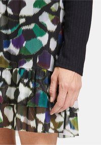 Multi-layered dress with a black ribbed long sleeve and a colorful, patterned flared hem featuring green, purple, and white accents.