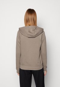 Brun huvad sweatshirt med en slät yta, ribbade ärmslut och nederkant. Har en enkel design utan synliga logotyper eller mönster.