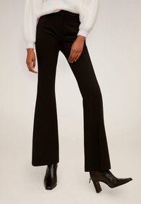 Pantalons noirs évasés avec une texture lisse et une taille ajustée. Associés à des bottes noires à talons aiguilles.