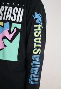Black long-sleeve t-shirt featuring graphic designs in pink, blue, and green, with "STASH" printed vertically in blue and yellow on the sleeve.
