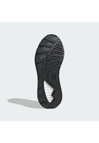 Suela de zapato atlético negra con textura de goma, que presenta ranuras para tracción y una sección de entresuela blanca con rayas horizontales.