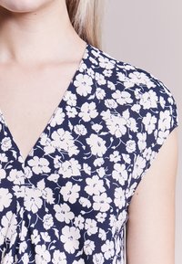 Blommig topp med marinblå bakgrund och vita blommor, V-ringning, korta ärmar och lätt tyg.
