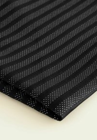 Tissu noir avec des rayures diagonales et de petits points blancs. Surface texturée avec un motif tissé, repliée soigneusement sur un bord.