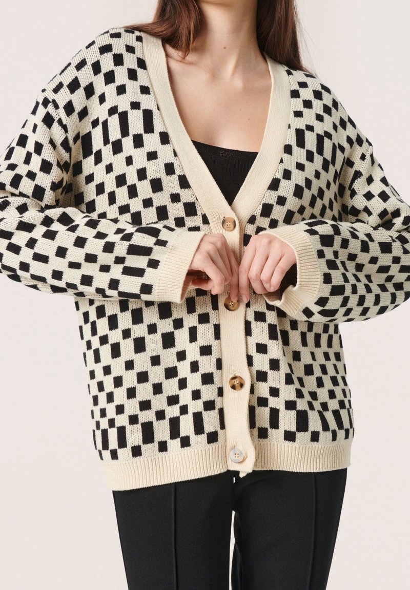 Krämfärgade och svarta rutiga koftan med V-ringning, knappstängning och ribbad ärm. Tillverkad i mjukt stickat material med en avslappnad passform.