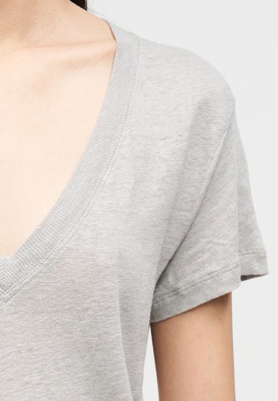 T-shirt gris à manches courtes et col en V, fabriqué en tissu léger, avec une texture douce et une coupe décontractée.