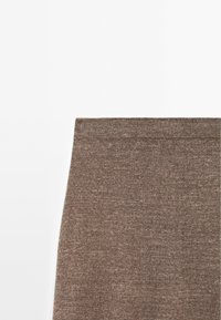 Section supérieure d'une jupe marron tricotée avec une ceinture ajustée sur un fond blanc uni.