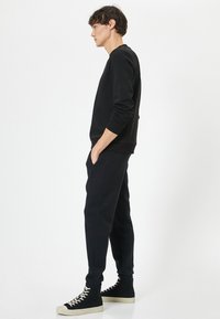 Sort bomulds sweatshirt med ribbede manchetter, parret med sorte tapered joggers. Båret med høje sorte sneakers med hvide accenter.
