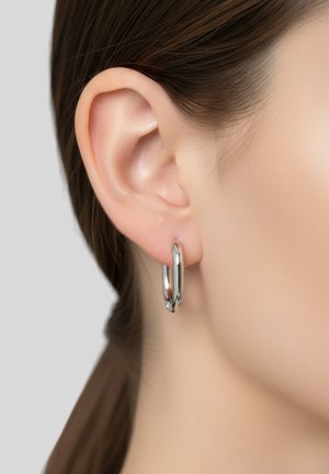 Des boucles d'oreilles en argent en forme de hoop pendent du lobe de l'oreille, présentant une surface lisse et brillante avec un design circulaire sans embellissements supplémentaires.