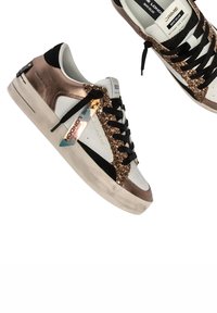 Sneakers bianchi con un design luccicante in rosa oro e glitter nero, lacci neri e una suola trasparente con un marchio su un'etichetta.