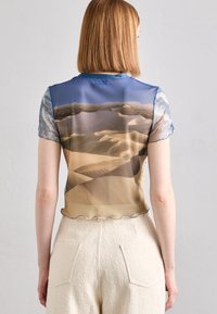 Gjennomsiktig blus med korte ermer i sanddyne-trykk i beige og blå toner; bølget kant, lett stoff og teksturerte ermer.