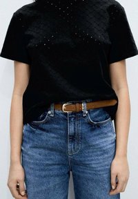 Black textured t-shirt with short sleeves, featuring small cut-out details; paired with high-waisted blue denim jeans and a brown leather belt.