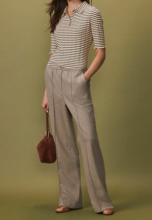 Gestreepte poloshirt in beige en zwart, gecombineerd met grijze wijde broek met een subtiele textuur, en een bruin handtasje. Soepele, relaxte pasvorm.