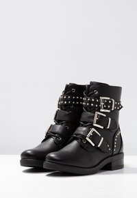 Stivaletti neri alla caviglia realizzati in pelle texturizzata, con multiple cinghie dotate di fibbie in argento e dettagli borchiati. Design con tacco basso a blocco.