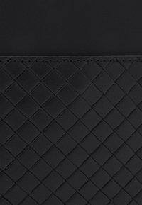 Czarna skórzana torba z fakturowanym splotem. Górna część gładka, z przeszytym szwem, podkreślającym kontrast materiałów.