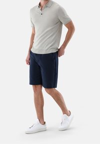 Jasnoszara koszulka polo z krótkim rękawem i trzema czarnymi guzikami, zestawiona z granatowymi szortami i białymi trampkami. Luźny, dopasowany krój.