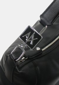 Borsa a mano in pelle nera con una chiusura a scatto in metallo argentato con le iniziali "AX" e una zip laterale. Texture liscia e forma compatta.