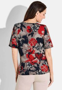 Beige shirt met korte mouwen met bloemmotief, voorzien van rode en marineblauwe bloemen. Zacht, gestructureerd materiaal met een ronde halslijn en een relaxte pasvorm.