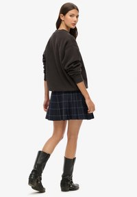 Sweat-shirt noir oversize, mini-jupe plissée en tartan bleu marine, bottes noires montantes jusqu'aux genoux. Matière douce, coupe décontractée et détail de surpiqûres bien visible.