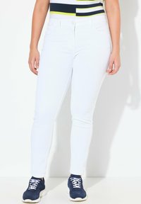 Bílé džíny skinny z denimu s hladkou texturou a přiléhavým střihem. Kombinované s námořnickými teniskami s bílými tkaničkami a robustní podrážkou.
