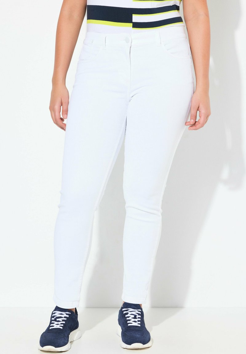 Bílé džíny skinny z denimu s hladkou texturou a přiléhavým střihem. Kombinované s námořnickými teniskami s bílými tkaničkami a robustní podrážkou.