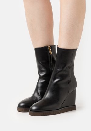 Black leather wedge ankle boots with a smooth finish, a zipper closure, and a textured brown sole. The design features a fitted silhouette.