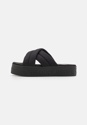 Czarne sandały na platformie z paskami z pikowanej tkaniny ułożonymi krzyżowo i napisem "TOMMY JEANS" wytłoczonym na boku grubej podeszwy.