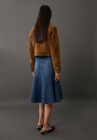 Ruskea mokkatakki, jonka pituus on vain lyhyt, yhdistettynä polvipituiseen siniseen farkkuhameeseen. Asusteessa on liehuva siluetti ja mustat paksupohjaiset kengät.