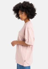 Lyserød oversized t-shirt med rund halsudskæring, afslappet pasform og korte ærmer; har en lille logodetalje på brystet.