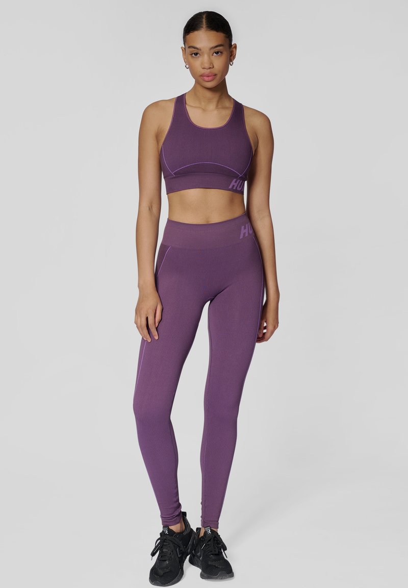 Fioletowy prążkowany zestaw sportowego topu w stylu crop oraz legginsów z kontrastowymi szwami, posiadający logo na pasku i elegancki design idealny do aktywności fizycznej.