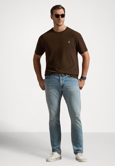 Καφέ βαμβακερό t-shirt με λαιμόκοψη crew, ανοιχτό μπλε τζιν με φθορές, λευκά αθλητικά παπούτσια και στρογγυλά μαύρα γυαλιά ηλίου. Casual εμφάνιση.