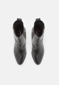 Bottes basses en cuir noir avec un bout pointu et une fermeture éclair latérale. Elles disposent d'une languette à l'arrière pour faciliter l'enfilage.