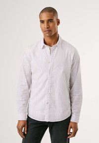 Camisa blanca con rayas rojas verticales, de mangas largas, con cuello abotonado y una textura sutil, combinada con jeans oscuros.