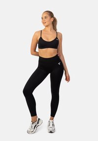 Zwarte sportbh en hoge taille legging gemaakt van rekbaar materiaal, met een gladde textuur. Sneakers hebben een ontwerp in wit en zwart.