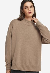Beige Strickpullover mit Stehkragen, überschnittenen Schultern und gerippten Bündchen. Weicher Stoff und lockere Passform für zusätzlichen Komfort.