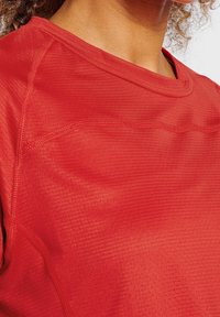Červené sportovní tričko z texturované, lehké tkaniny. Má kulatý výstřih a jemné žebrované vzory po celém povrchu.