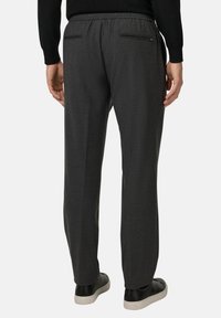 Pilkos pritaikytos kelnės su elastine juosta, užpakalinėmis kišenėmis su užtrauktukais, lygaus audinio tekstūra ir tiesiomis kojomis. Dėvimos su juodais sportbačiais.