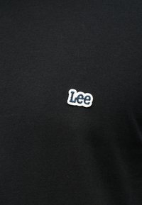 Μαύρο ύφασμα με μικρό λευκό και ναυτικό μπλε κεντημένο λογότυπο "Lee" κεντραρισμένο στην περιοχή του στήθους.