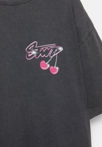 T-shirt noir en coton avec un design graphique arborant le mot "Swag" en rose et deux cerises roses. Manches courtes et col rond.
