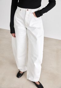 Witte wijde jeans van denimstof, met een hoge taille, een knoopsluiting en zijzakken, gecombineerd met een zwarte top met lange mouwen.