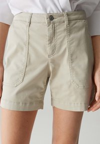 Shorts beiges en mélange de coton, présentant une coupe droite, deux poches avant et une fermeture à bouton. Texture lisse et bords soigneusement ourlés.