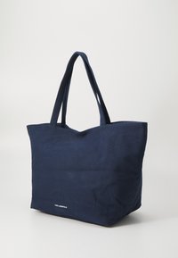 Saco de lona azul-marinho com alças duplas, formato retangular, tecido texturizado e um pequeno logo branco na parte inferior da frente.