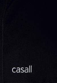 Zwart sportief stof met een gladde textuur, voorzien van een wit "casall" logo. Naaddetails lopen langs de rand en benadrukken een getailleerd ontwerp.