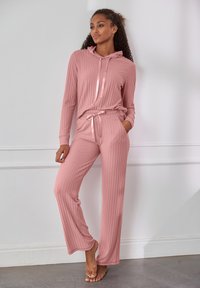 Lichtroze geribbeld loungepak met een capuchontop met een voorpanneel en bijpassende joggingsbroek met trekkoord, beide van zachte stof.