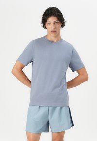 Lyseblå bomulds T-shirt med rund halsudskæring, korte ærmer og løs pasform, bæres med lyseblå shorts med et marineblåt sidelæg.