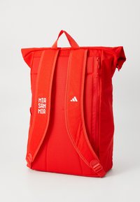 Rød rullesekk med nettingstropper og sideglidelås-lomme. Har "MIA SAN MIA" og Adidas-logo i hvitt på forsiden. Slitesterkt stoff.