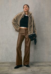 Faux fur zip-up jakke i beige, cropped sort top, brune læder flaired bukser og sorte hæle støvler. Holder en sort handvogn.