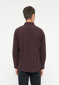 Camicia di flanella a scacchi grigio scuro con motivo a griglia rossa, maniche lunghe con polsini a bottone e orlo curvo. Tessuto morbido, design casual.