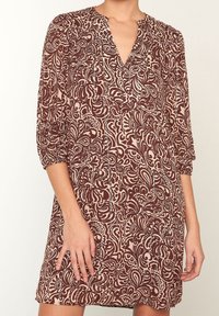 Mörkröd och beige mönstrad klänning med V-ringning, trekvartsärmar och ett lätt tyg, som har intrikata snurrande mönster.