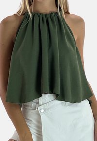 Top de halter verde hecho de tela suave, con escote fruncido y un diseño suelto y fluido. Combinado con pantalones cortos de mezclilla blancos.