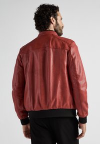 Rød læderjakke med en glat tekstur, ribbede sorte manchetter og kant, samt et klassisk bomberdesign. Bagfra ses rene sømme og minimal detaljering.